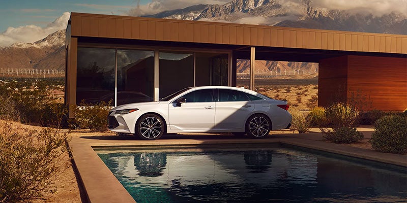 A white 2022 Toyota Avalon is parked outside a house.