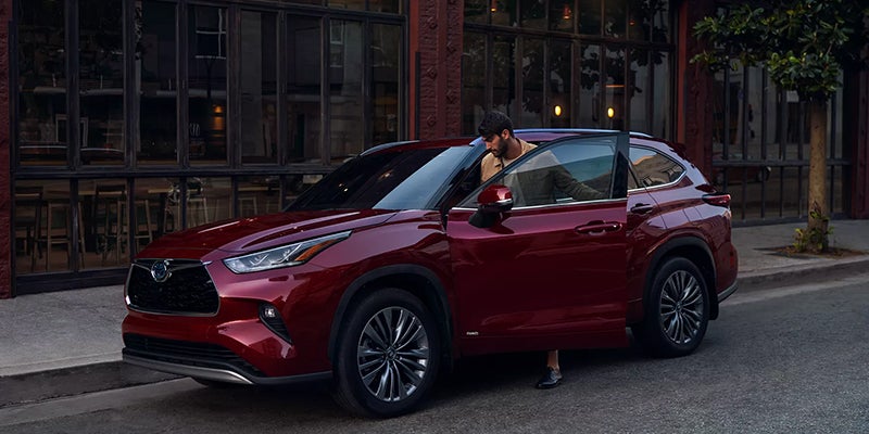 A man gets into a red Toyota Highlander parked on a city street