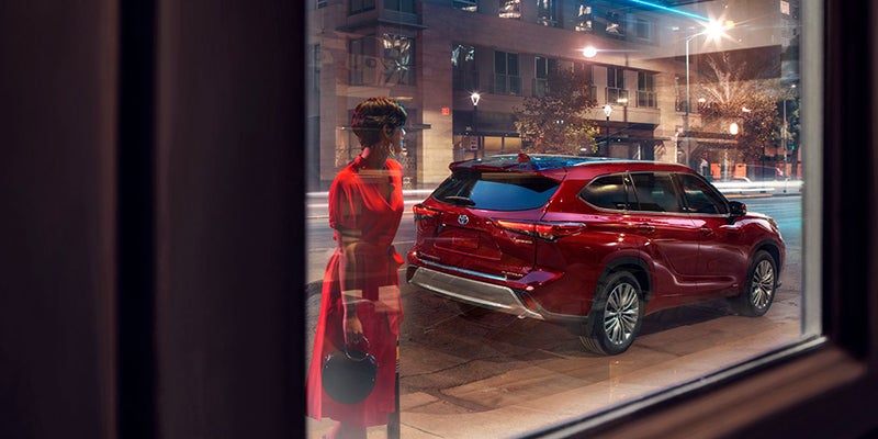 A woman peers into a shop window at night. A red Toyota Highlander is parked on the street.