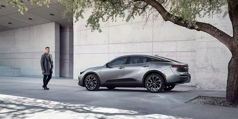 A silver 2023 Toyota Crown parked next to a concrete building under a tree.