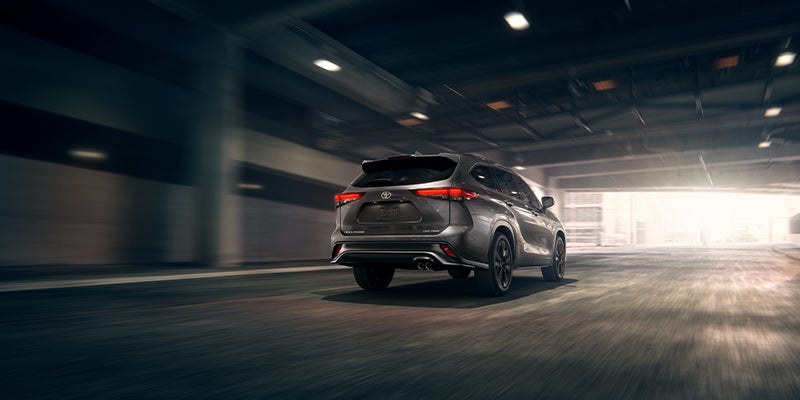 A silver 2023 Toyota Highlander drives away underneath a highway overpass.