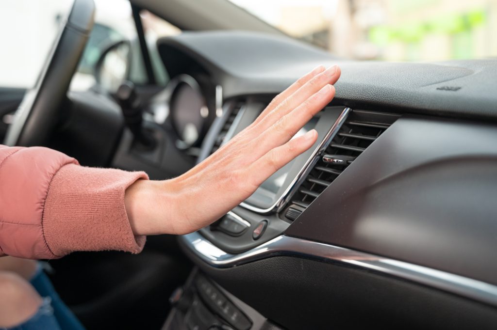 A person checking airflow from a car air vent inside a modern vehicle.