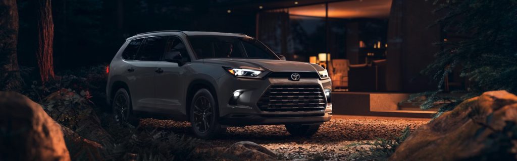 2026 Toyota Grand Highlander Hybrid SUV showcased in a residential nighttime setting, emphasizing fuel-efficient hybrid performance, family-friendly space, advanced safety features, and upscale comfort.