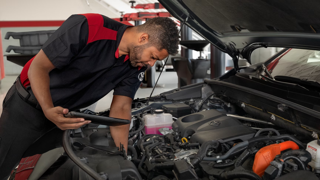 Toyota-certified technician performing vehicle maintenance and engine diagnostics using a tablet in a professional auto service center, highlighting expert repair and advanced technology.