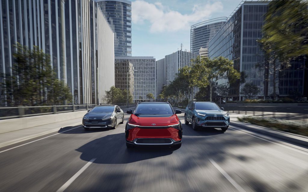 Three Toyota vehicles driving through a modern city street, featuring a red crossover SUV in the center flanked by a sedan and SUV.